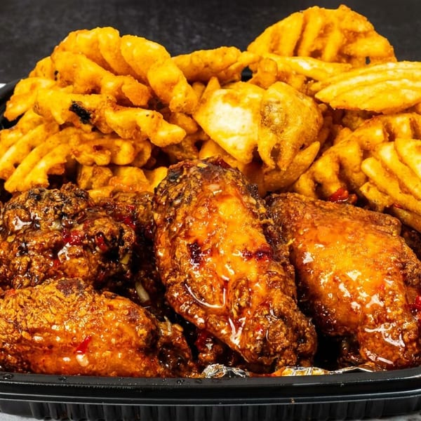 Black takeout container filled with glazed chicken wings and waffle fries on branded paper.