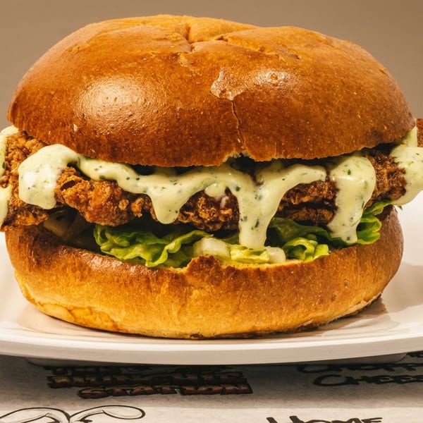 Crispy fried chicken sandwich with lettuce and green sauce on a golden bun.