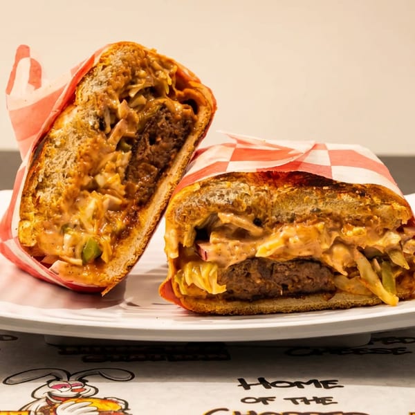 Two halves of a chopped cheese sandwich, wrapped in checkered paper, on a white plate.